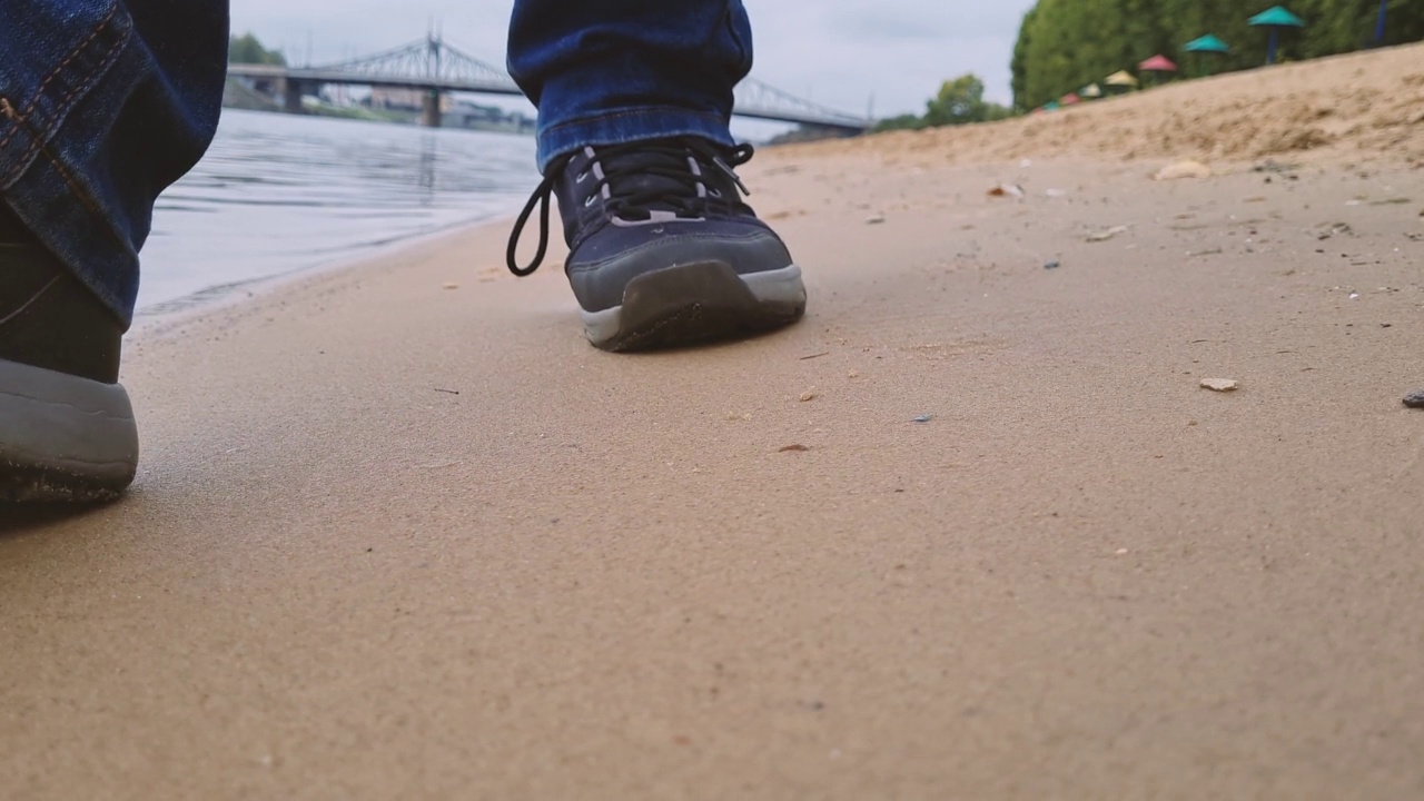 男人的脚沿着海滩走。一个穿着运动鞋的男人沿着海岸走。脚印在沙滩上。视频素材
