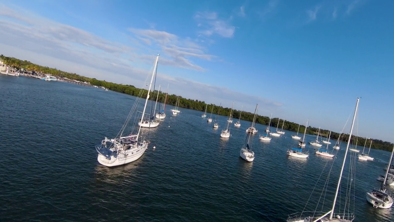 无人机在日落时飞过码头，海湾上有帆船，背景是迈阿密的天际线视频素材