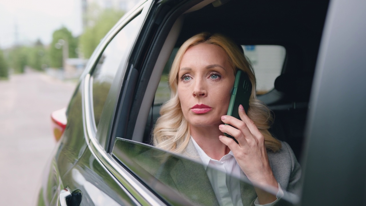 美丽的金发女游客在出租车或私人汽车旅行，在智能手机上聊天，通过车窗观看视频素材
