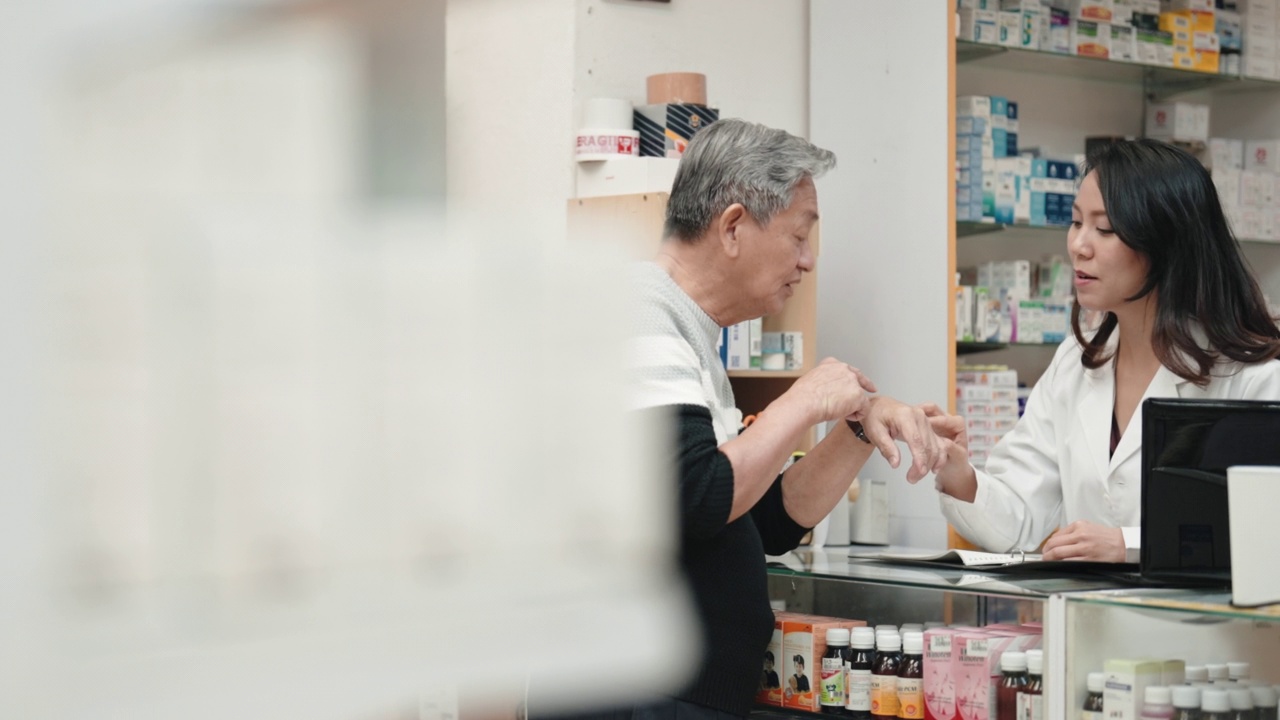 亚洲华裔女药剂师在药房柜台向年长的男性顾客解释视频下载