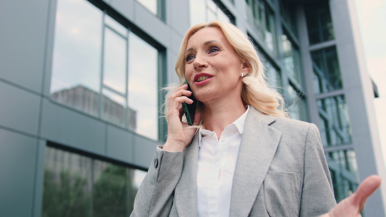 商务迷人的成熟女性穿着商务风格在户外用手机交谈，在城市的商业中心视频素材