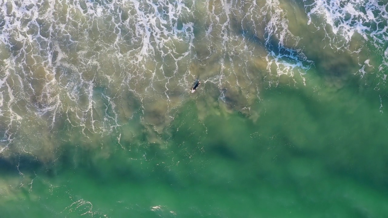 无人机在一名穿着黑色泳衣的冲浪者上方飞行视频素材