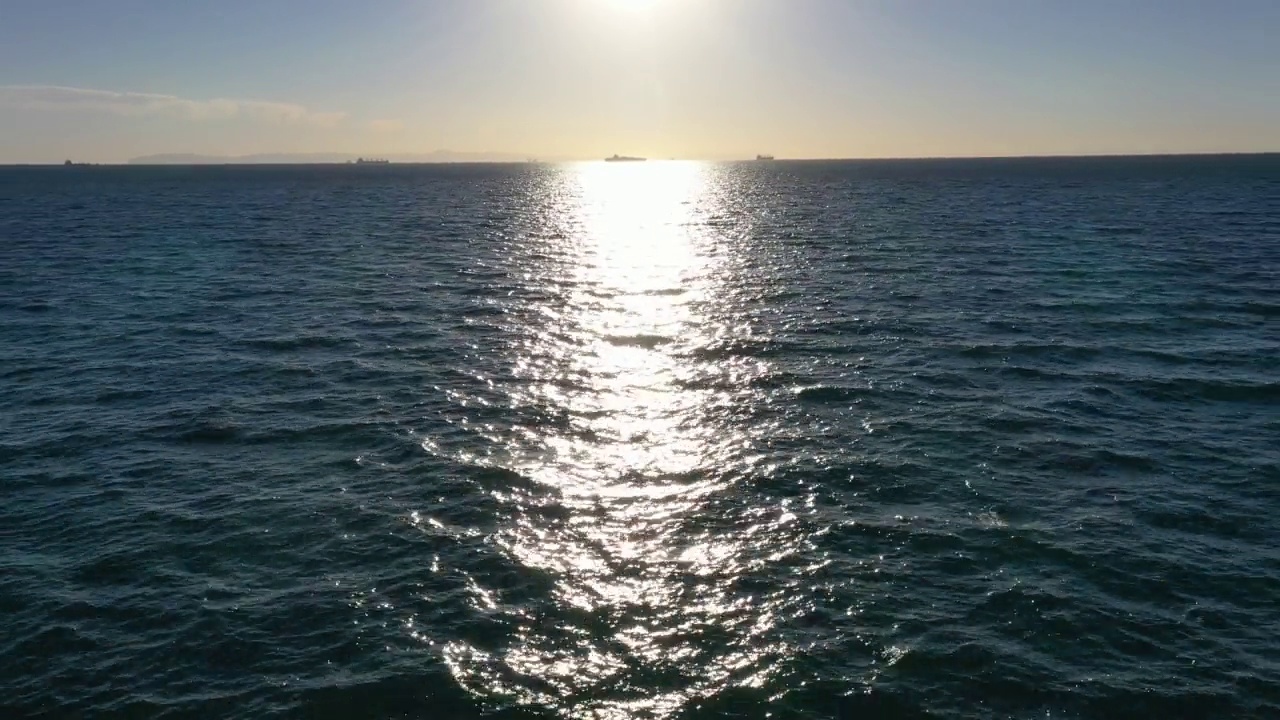 无人机在太平洋上空快速飞行，远离地平线，太阳和船只在远处视频素材