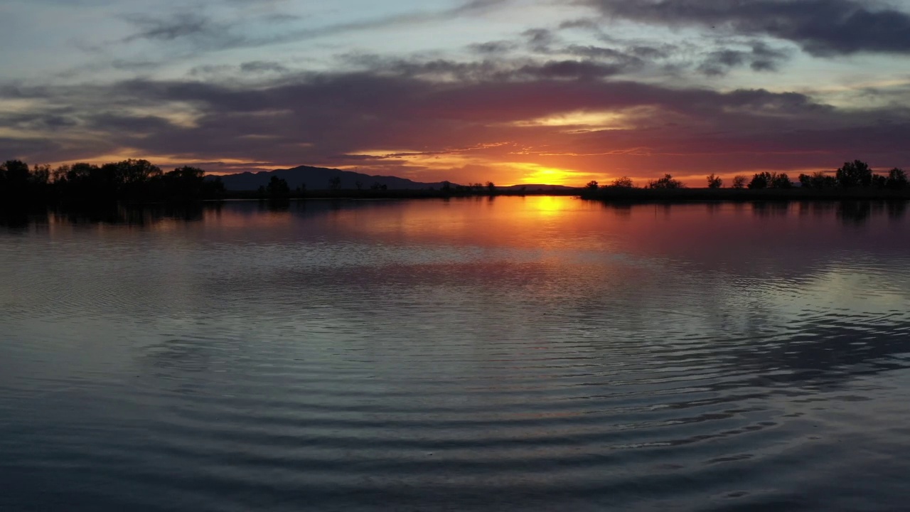 在日落的湖面上向后飞行的无人机视频素材