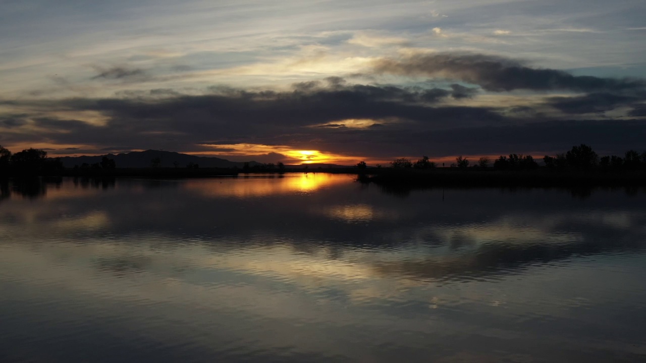 日落时无人机在湖面上空盘旋，太阳反射在水面上视频素材