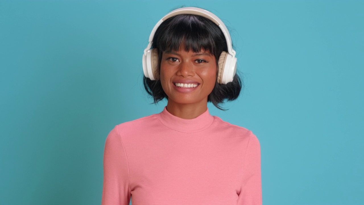 年轻的混血女子微笑着，戴着耳机在蓝色的墙上听音乐视频素材