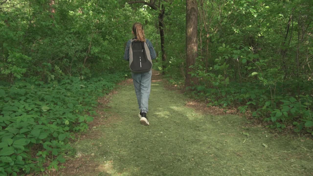 一个学龄女孩肩上背着背包，独自穿过森林。她回头一看，发现有危险，赶紧跑开了。视频素材