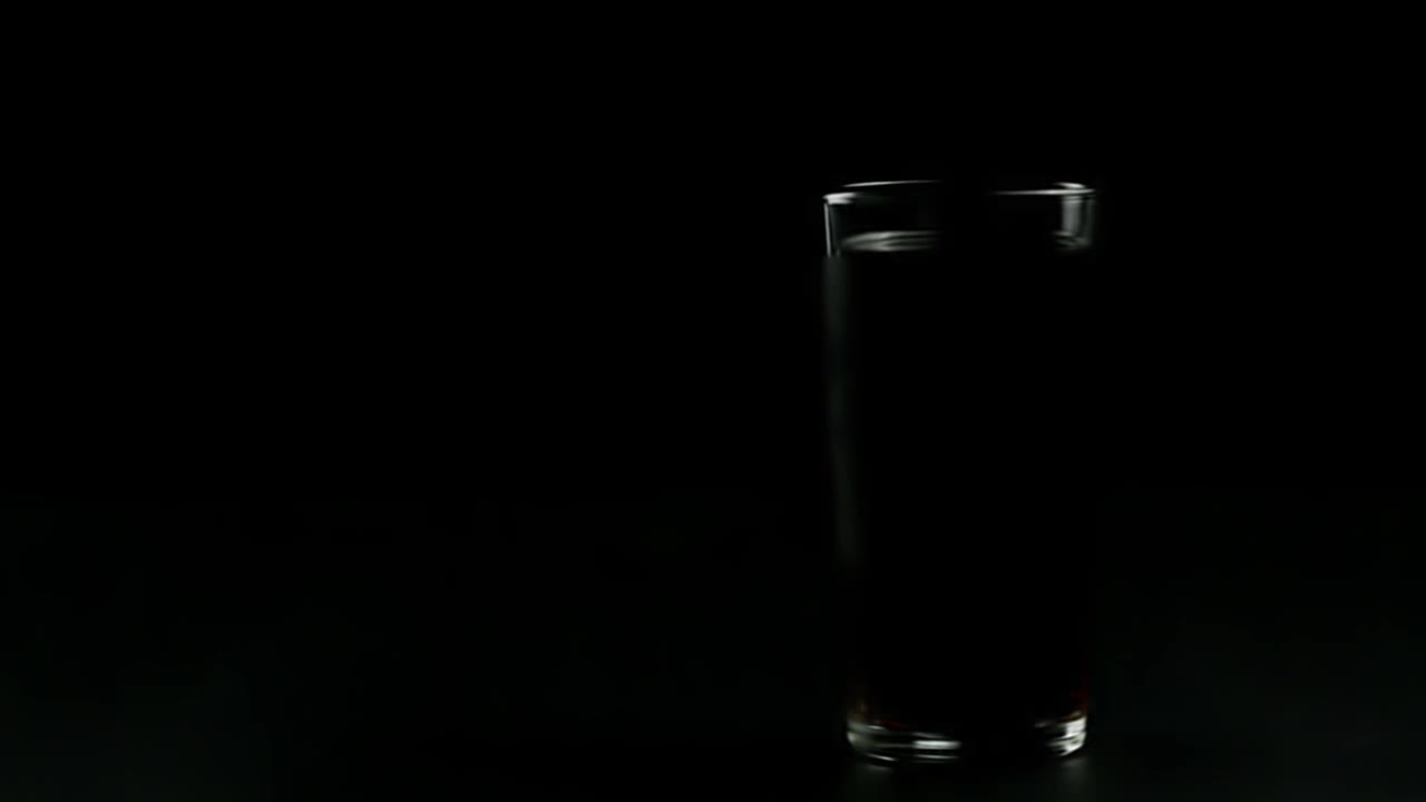 一个装满黑色苏打水的玻璃杯，在黑色的背景上，玻璃杯附近有液滴视频下载
