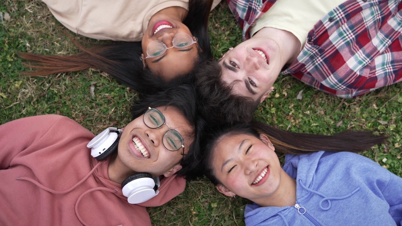 与朋友度过美好的时光-俯视一群快乐微笑的少年学生躺在草地上视频下载