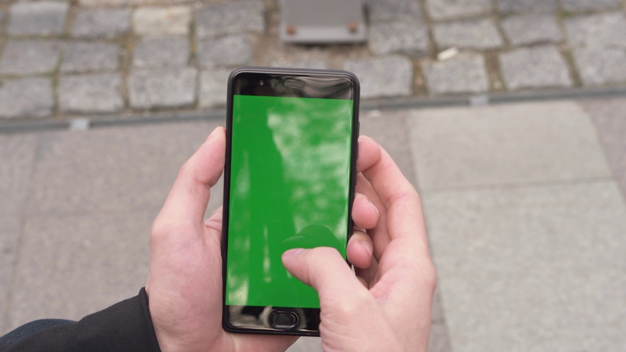 绿色屏幕的智能手机特写。彩色键在手机上，双手使用设备。背景是外面的街道视频素材