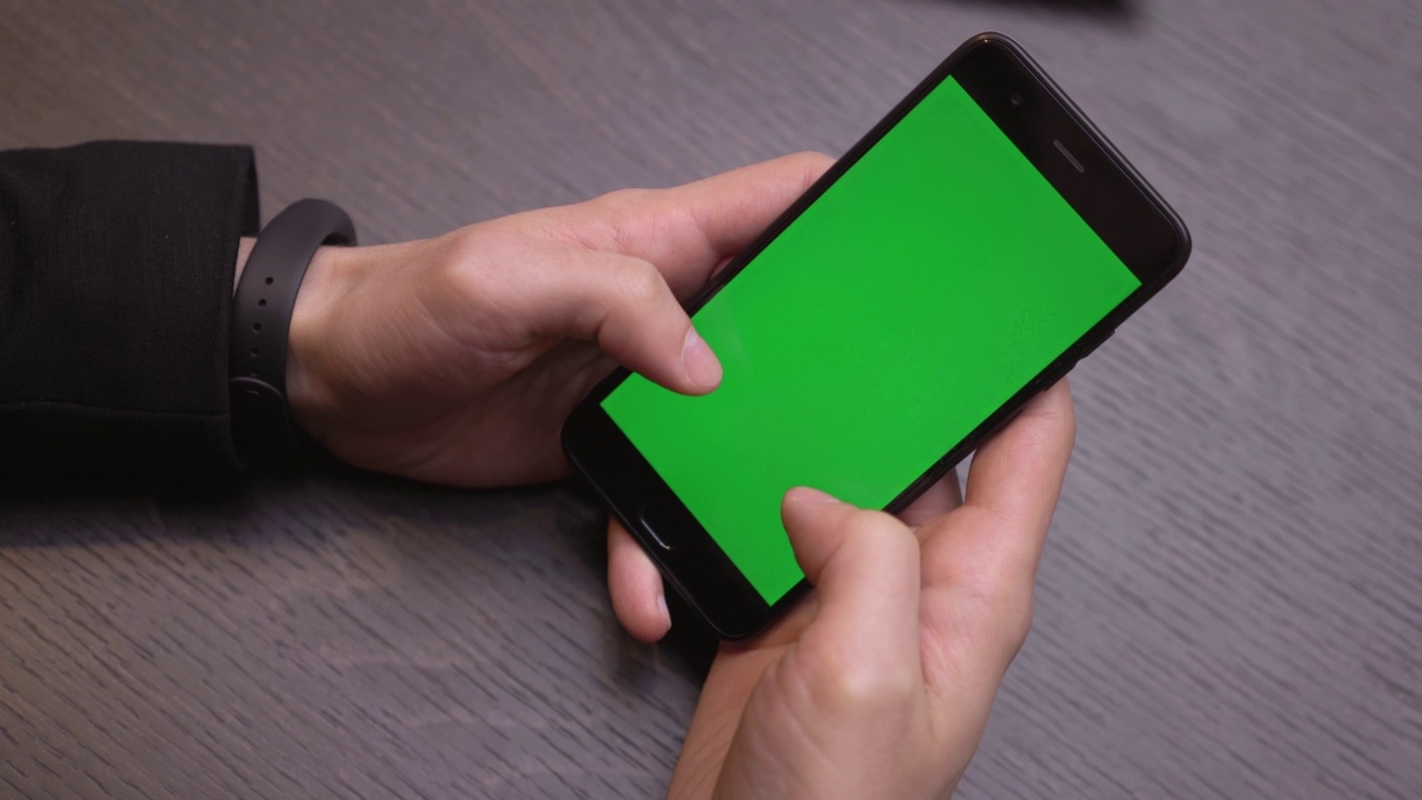 绿色屏幕的智能手机特写。彩色键在手机上，双手使用设备。桌子上的背景视频素材