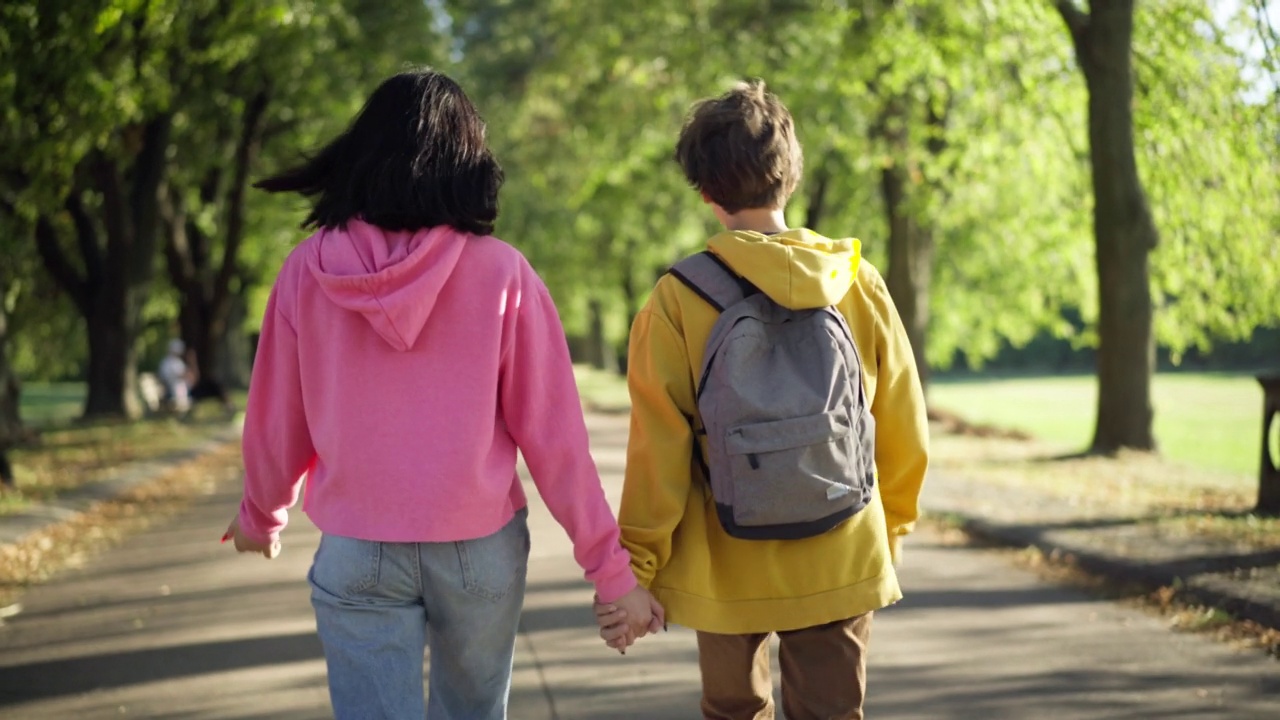 后视图十几岁的夫妇牵手散步在公园小巷的阳光。幸福可爱的白人青少年男友和女友在户外散步。浪漫和初恋的概念。视频下载