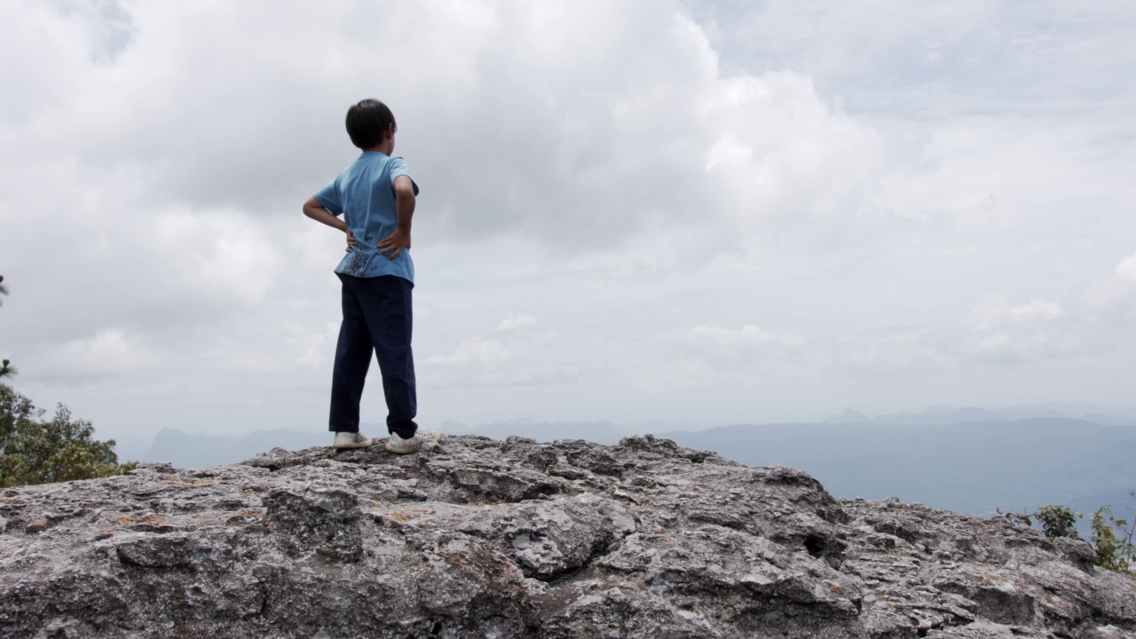 ฺ男孩高举双臂站在悬崖顶上。视频素材