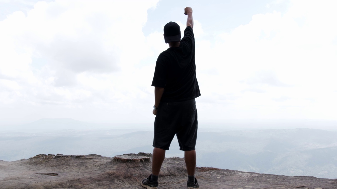 一个人高举双臂站在悬崖上。视频素材