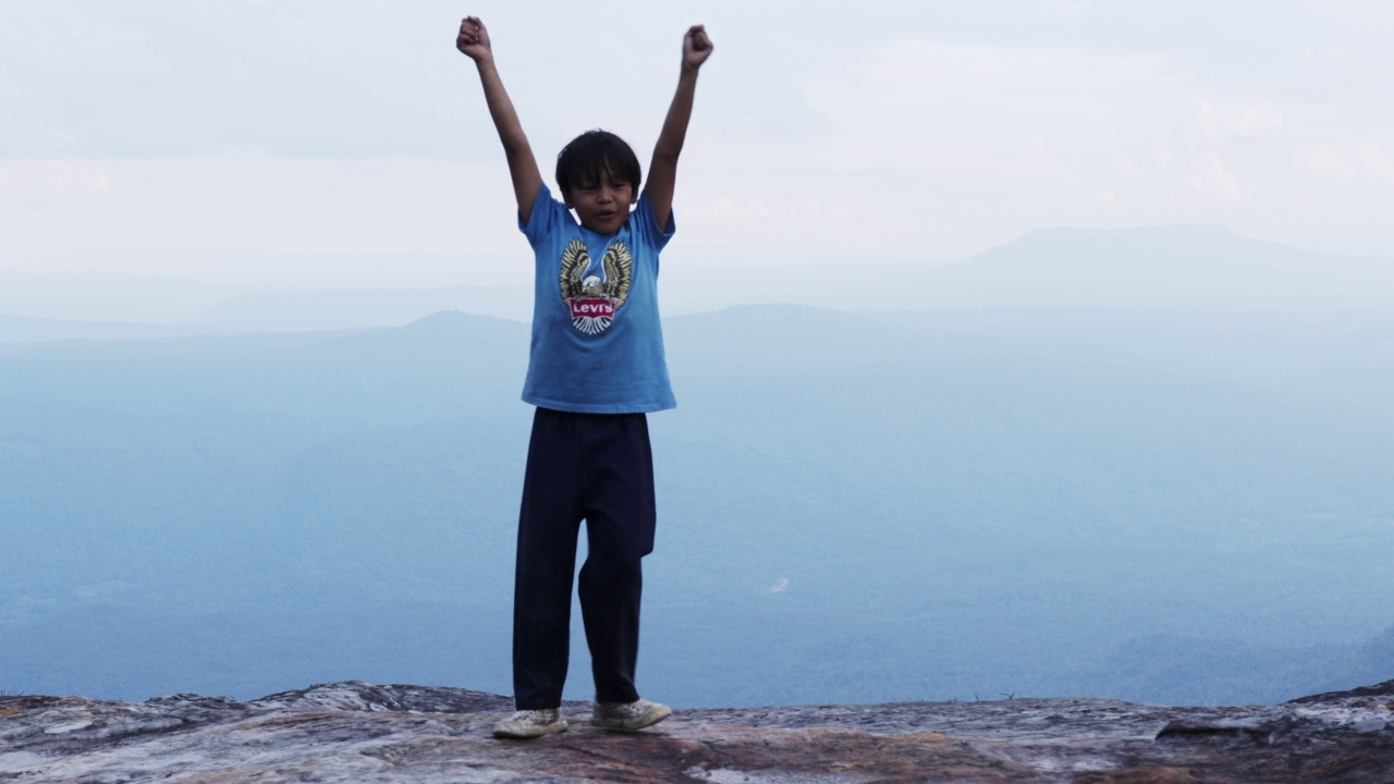 ฺ男孩高举双臂站在悬崖顶上。视频素材