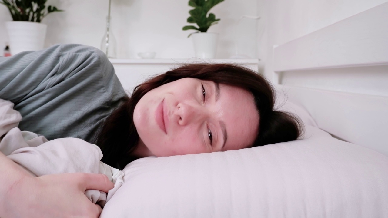 一个美丽的女人在床上醒来，对着相机微笑的特写镜头视频素材