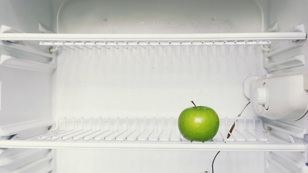 一个男人的手打开空冰箱，拿了一个青苹果。概念4k原始视频。经济危机，食物短缺，贫穷。视频下载