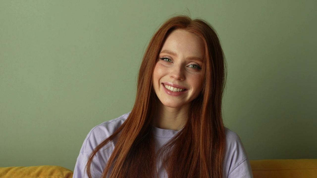 美丽开朗的年轻红发女人的肖像微笑着看着相机在光墙的背景。视频素材