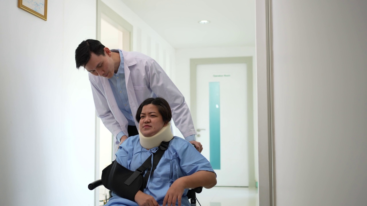 亚洲女性轮椅患者意外后与医生交谈，理疗师向患者解释如何康复，外科医生推着轮椅上的患者，意外受伤疼痛视频下载