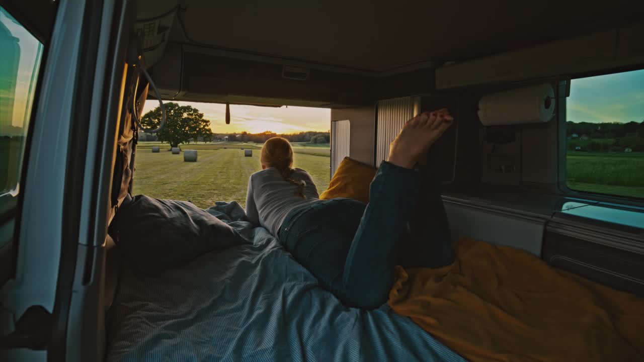 在日落时分，DL女士从停在草地上的露营车的小木屋里欣赏风景视频下载