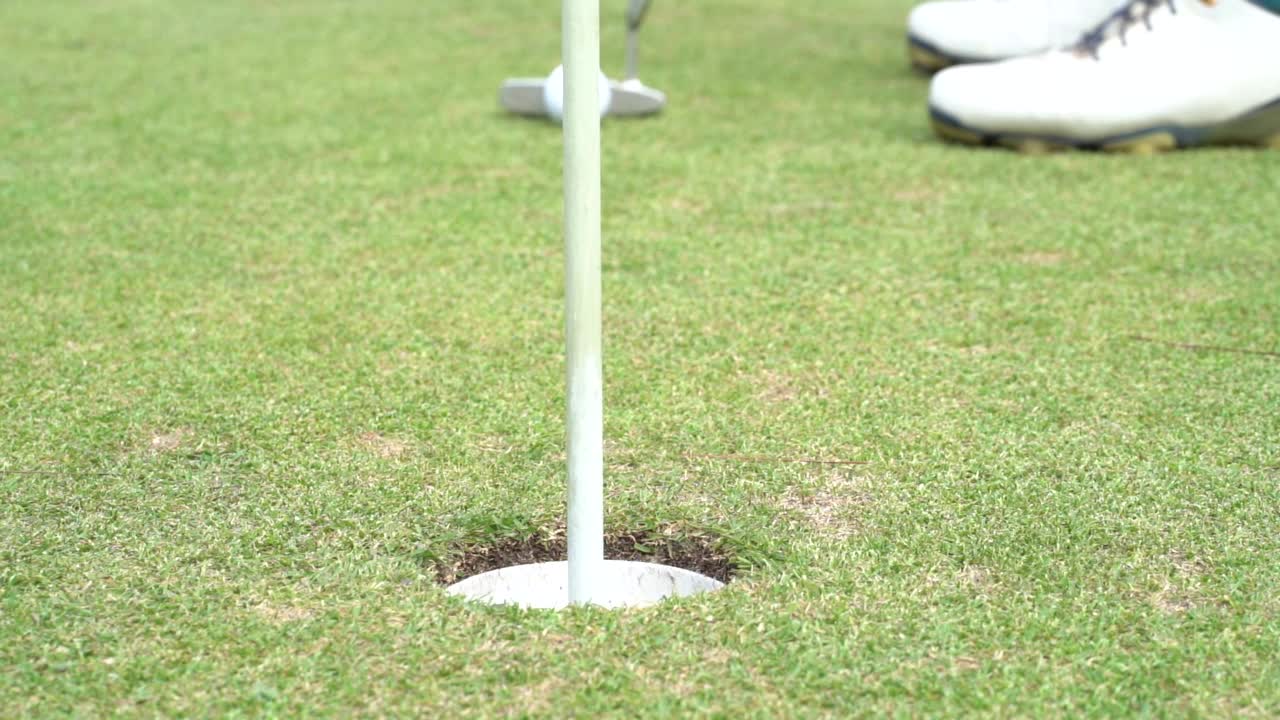 在高尔夫球场的果岭上，将高尔夫球打入洞中以获得小鸟球得分视频素材