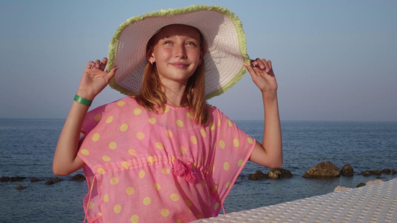 快乐的十几岁女孩在夏天的帽子享受阳光的海滩。肖像微笑的十几岁的女孩在蓝色的海洋景观，而海滩季节。视频下载