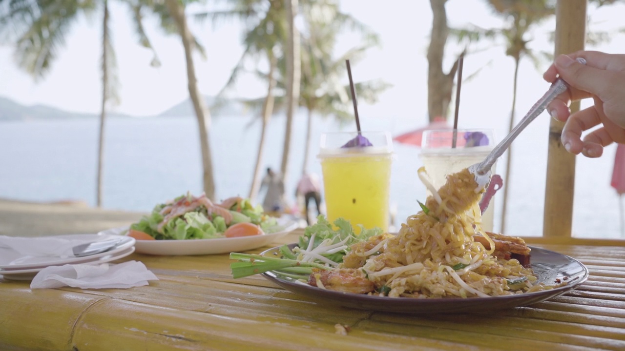 顶视图泰式炒河虾盘椰子树海滨背景。泰国著名的食物。视频下载