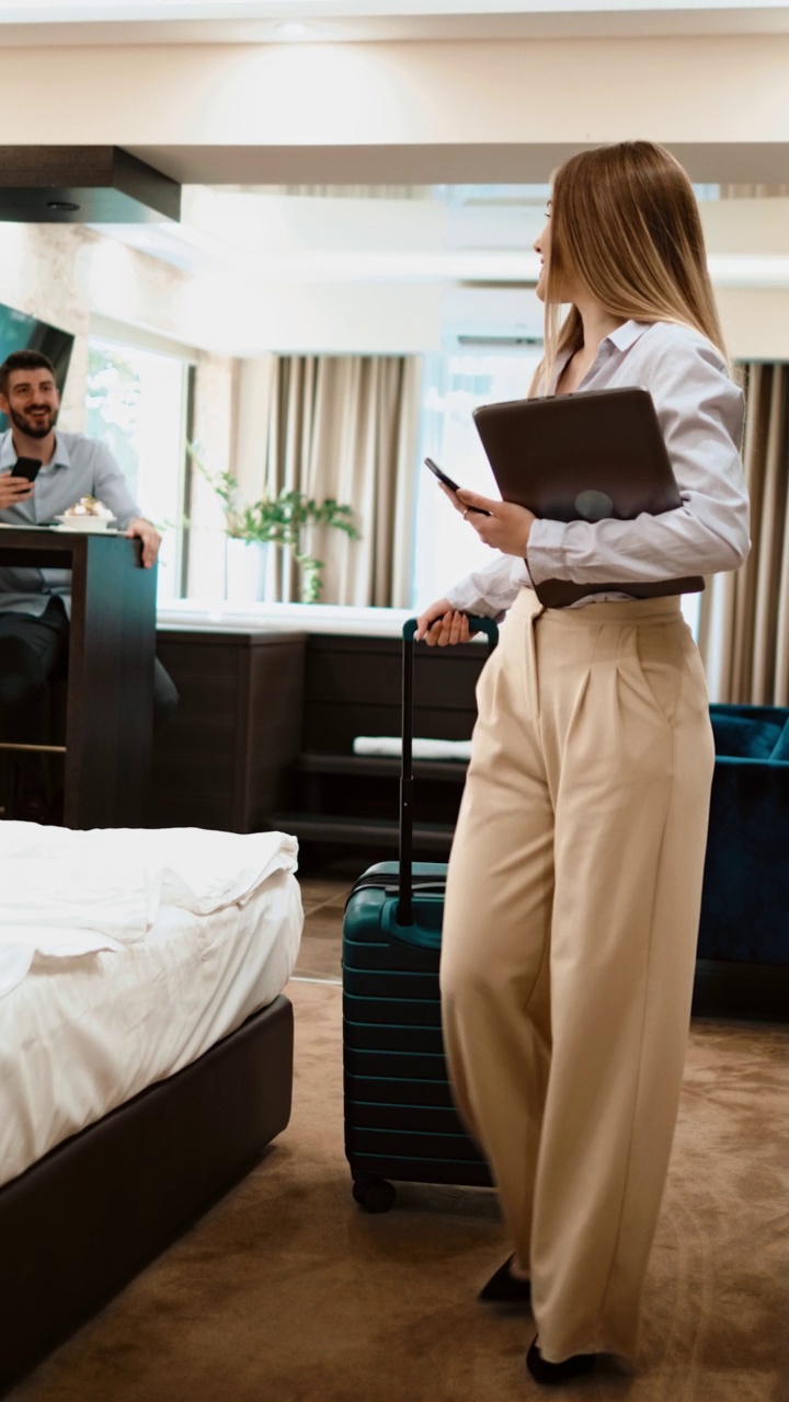 年轻的女商人带着手提电脑和行李箱离开酒店房间，向同事打招呼。商务青年离开酒店房间视频下载