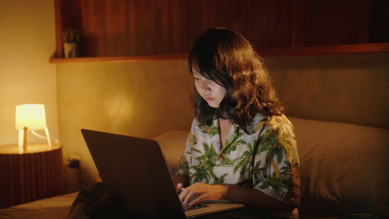 年轻的亚洲女性在床上享受假期，在键盘上打字，使用笔记本电脑触控板。视频素材