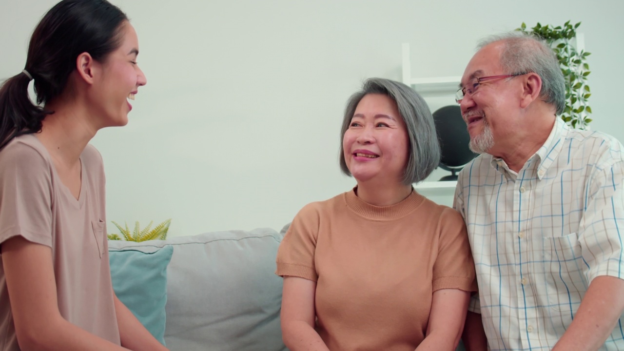 亚洲老人在家里客厅的沙发上与女儿谈笑风生的快乐家庭时光。一个充满爱和温暖的家庭，年迈的夫妇带着美丽的十几岁的女儿在周末视频素材