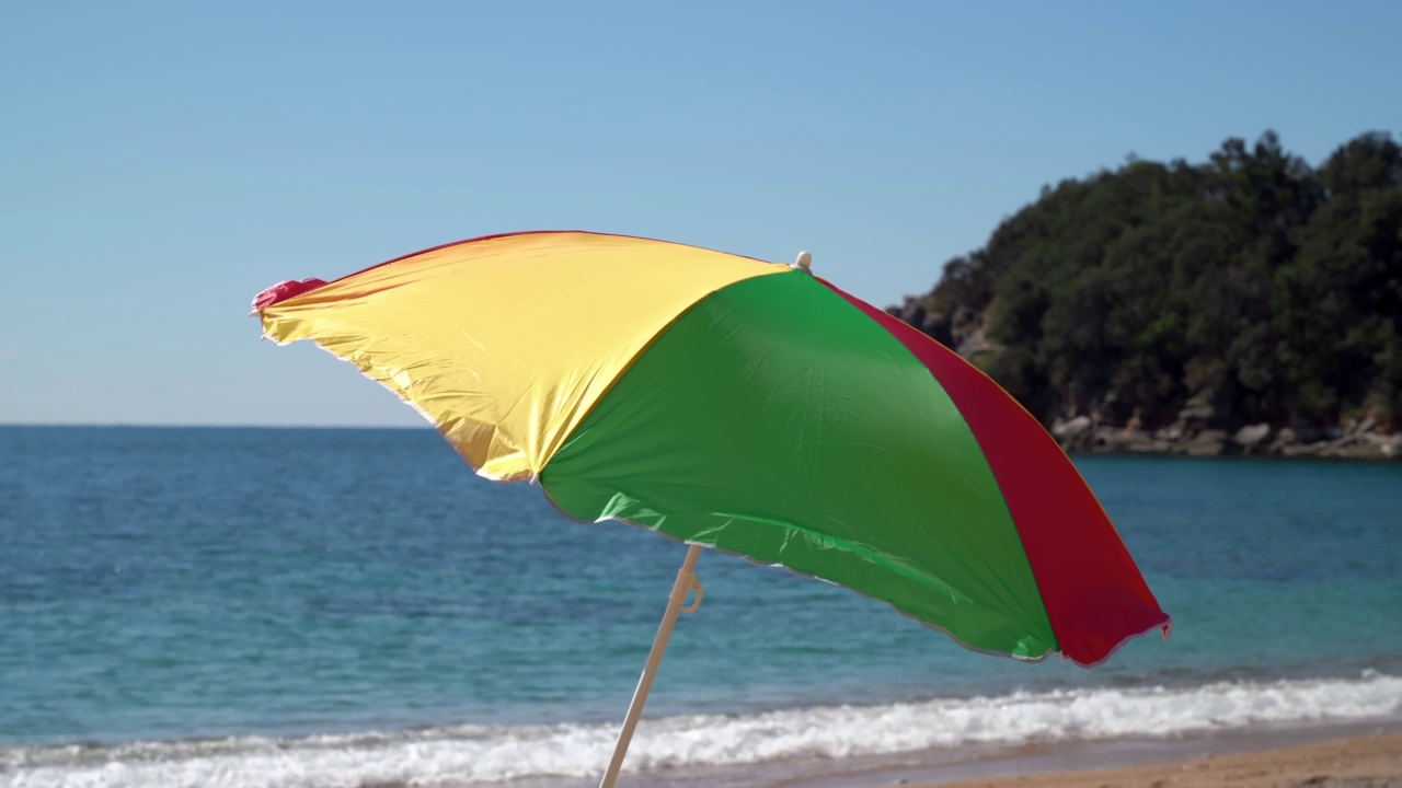 海滩上有明亮的遮阳伞，背景是明亮的蓝色天空和海浪。旅游及旅游概念视频素材