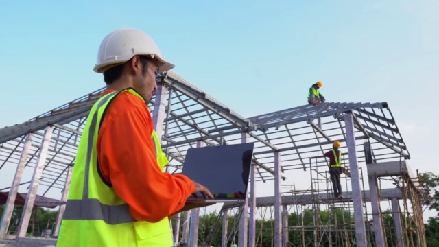 工程师技术员使用笔记本电脑观看工人钢屋顶结构施工。团队合作的概念。视频素材