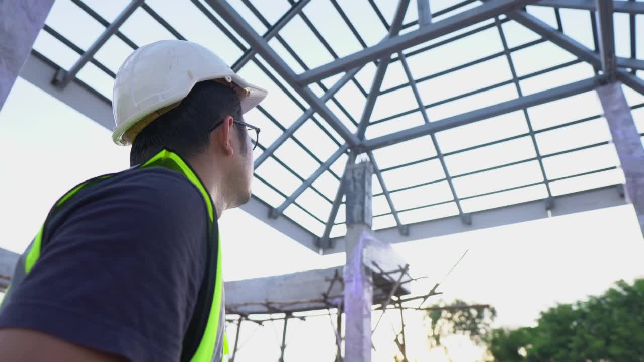 在房屋建筑工地，一名工程技术人员使用蓝图纸观察检查钢屋顶结构。视频素材