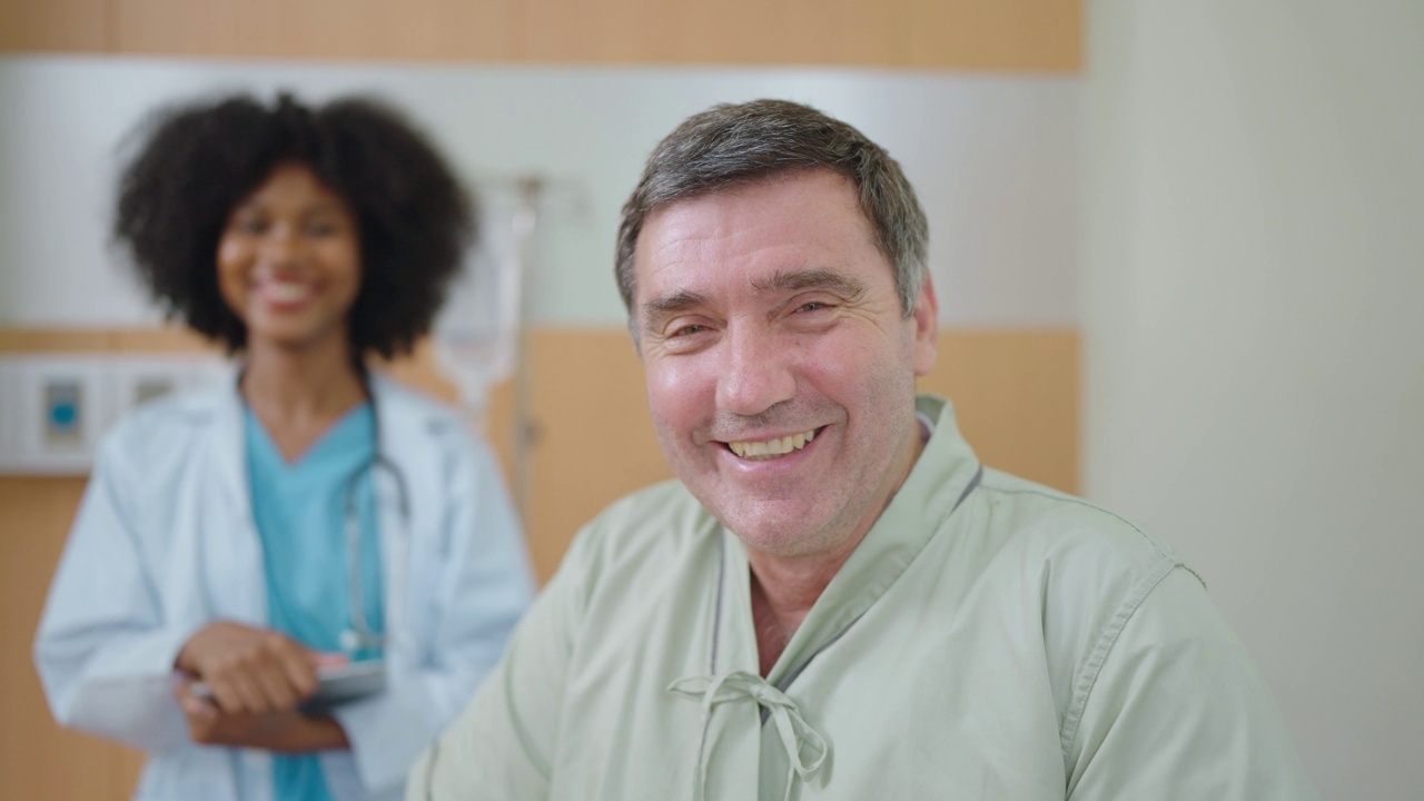 微笑着接受治疗的病人看着镜头，非裔美国黑人女医生站在病房的后面。老年人保健理念。视频素材