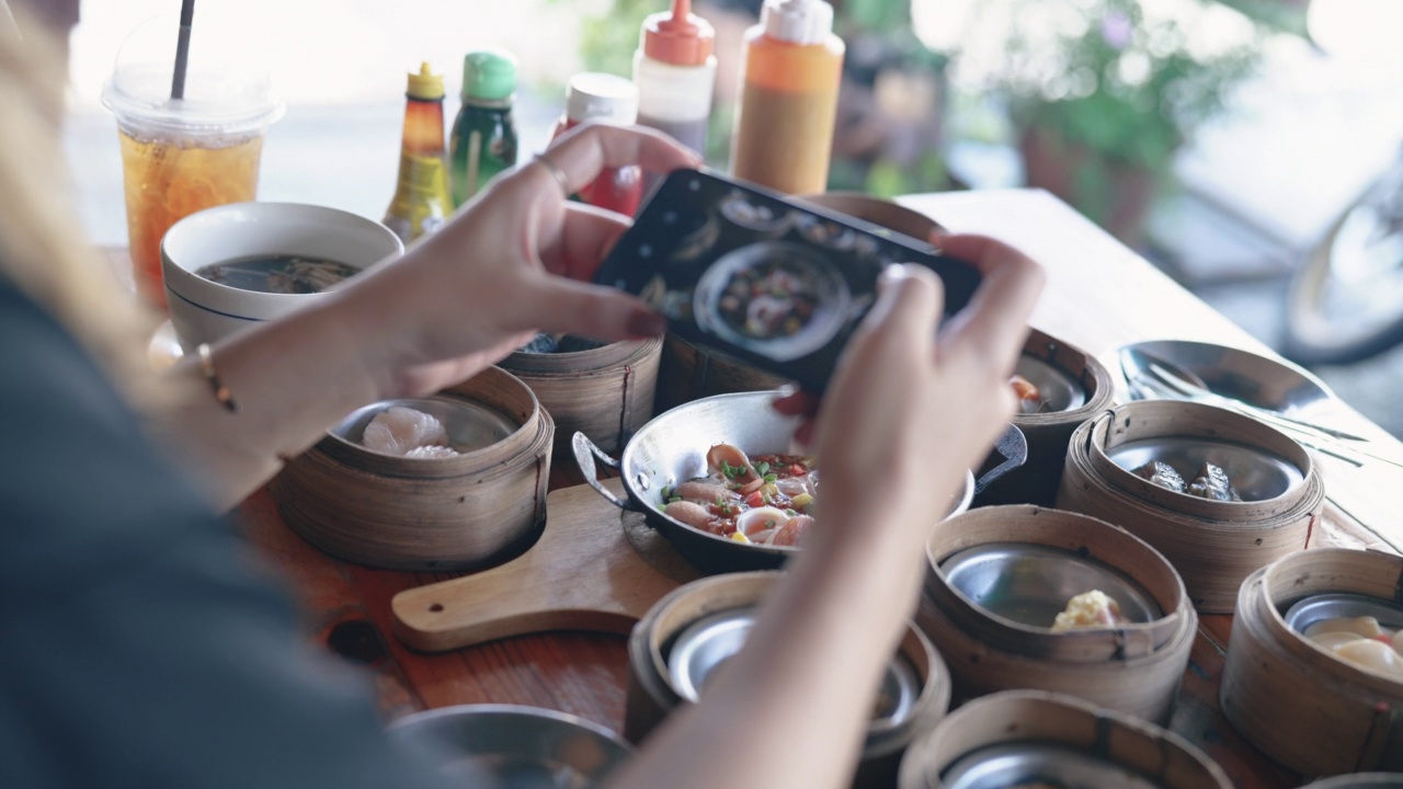 亚洲女人用手机拍桌子上的食物。视频下载