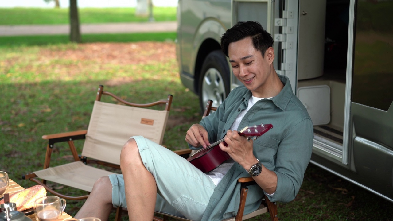 一名亚洲男子在露营车旁野餐时弹奏尤克里里视频素材