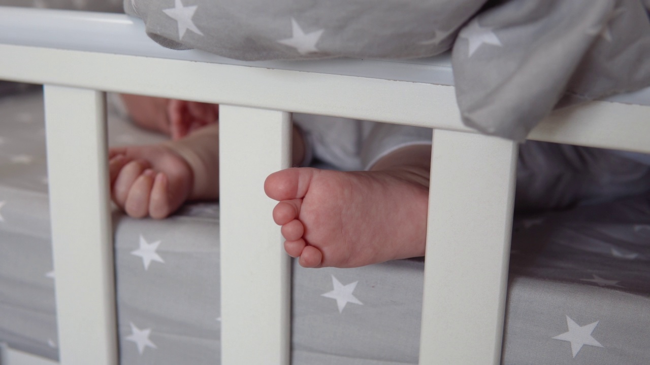 从婴儿床的毯子下面可以看到睡着的婴儿的胳膊和腿视频下载