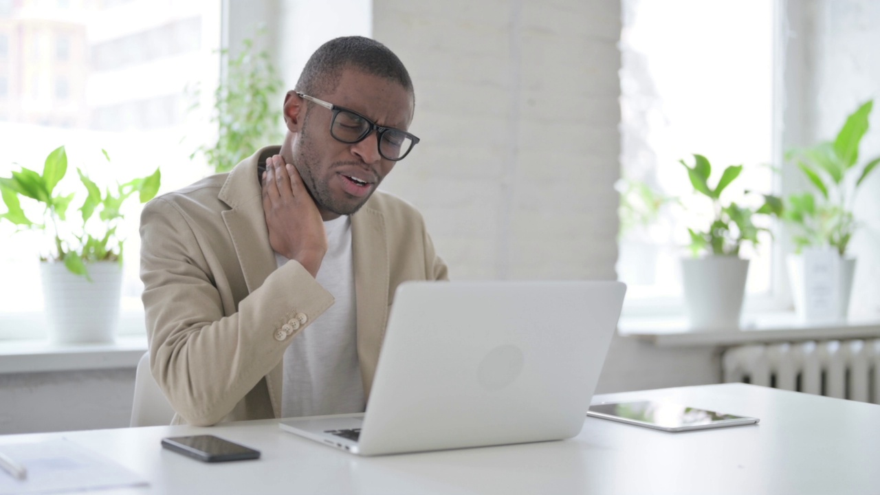 非洲男子在办公室使用笔记本电脑时颈部疼痛视频下载