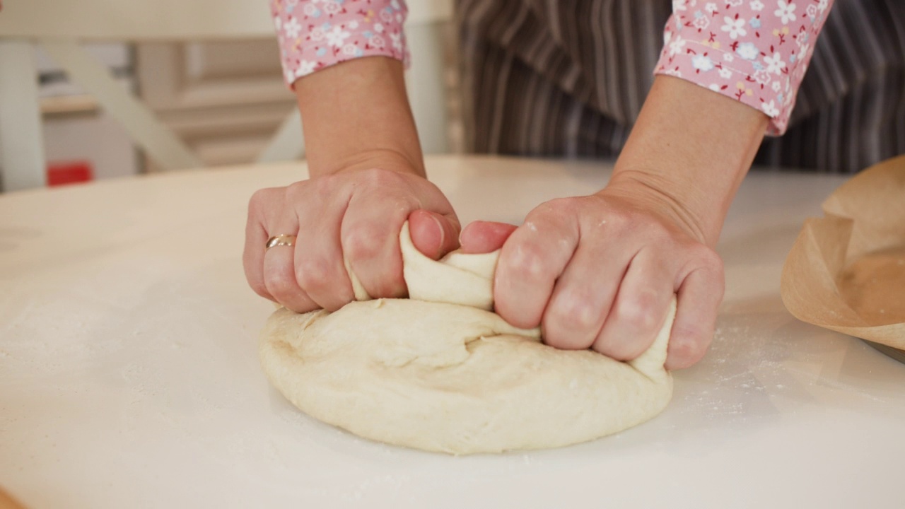 特写女性在厨房桌子上揉面团的手。女面包师在厨房里为自制烘焙食品准备面团。视频素材