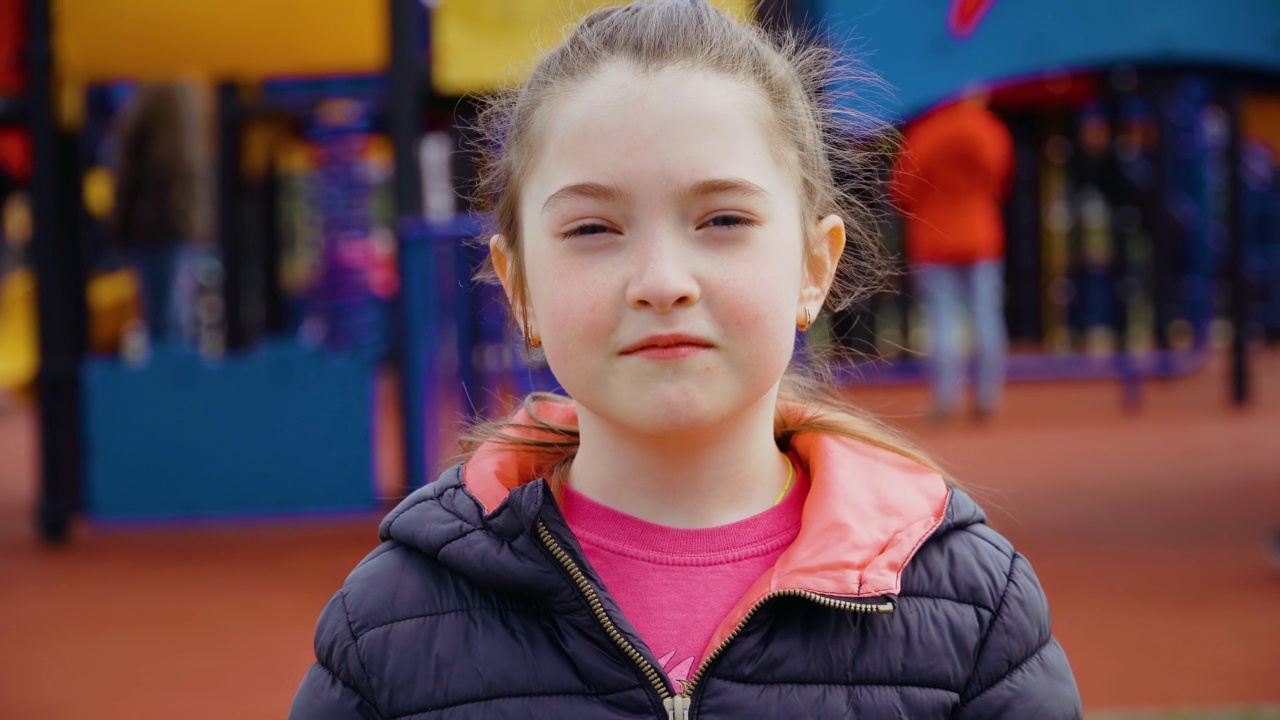 悲伤沮丧的小女孩的肖像看着相机在娱乐公园的背景儿童游乐场视频素材