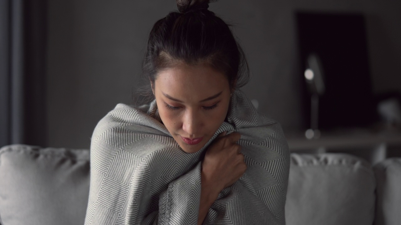 亚洲妇女生病了，在家里的沙发上用纸巾打喷嚏。女性患感冒擤鼻涕。寒热概念。视频素材