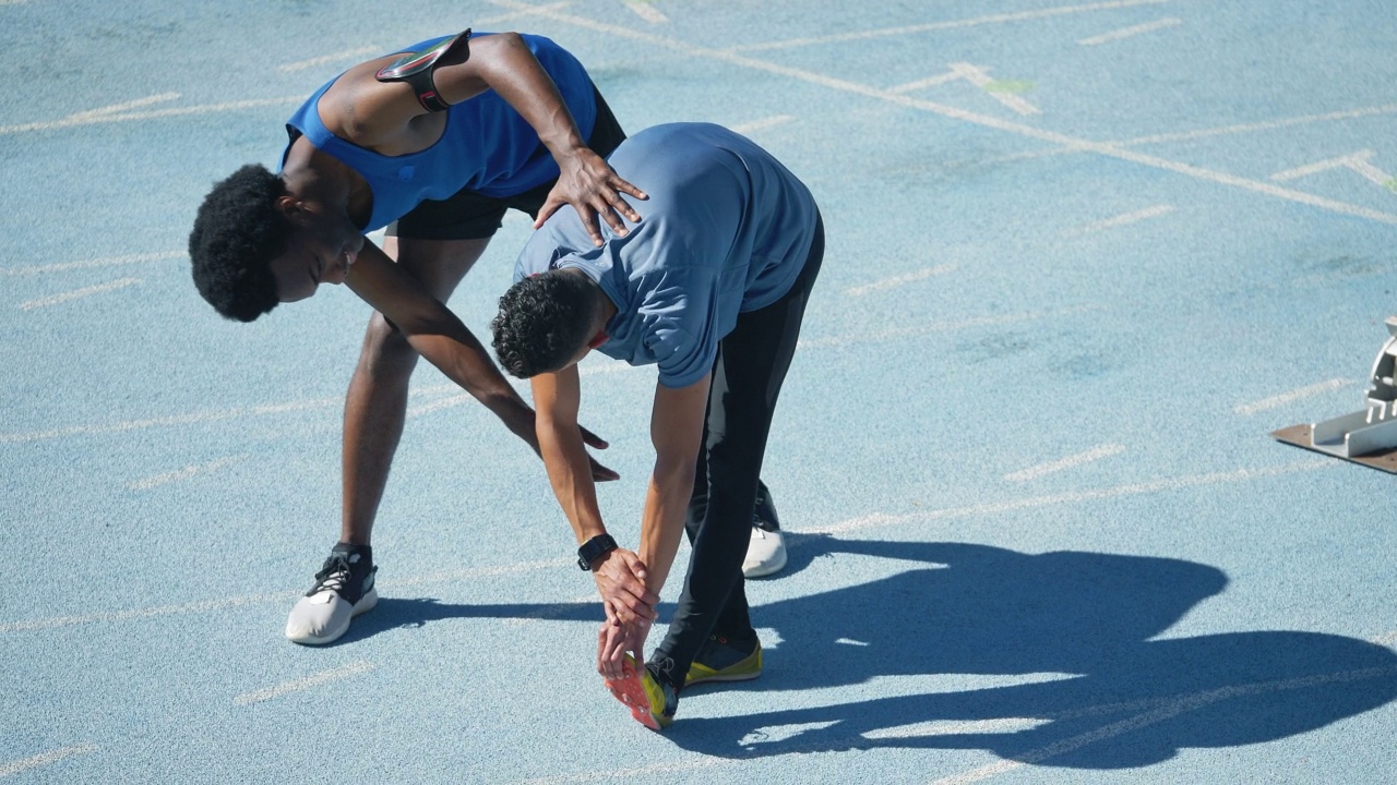 年轻的男运动员帮助队友在阳光灿烂的跑道上伸展视频素材