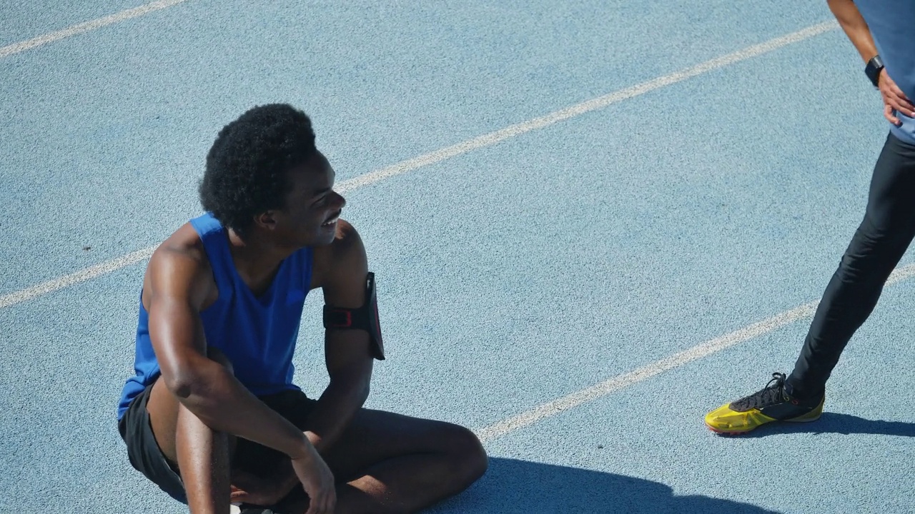 年轻的男性田径运动员在跑道上伸展和交谈视频素材