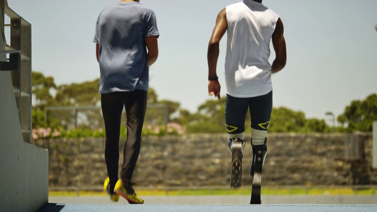年轻的男性截肢运动员和队友正在跑道上奔跑视频素材