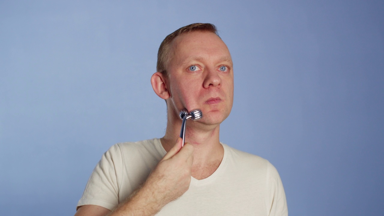 健康皮肤男子肖像正在用面部按摩辊进行面部按摩视频下载