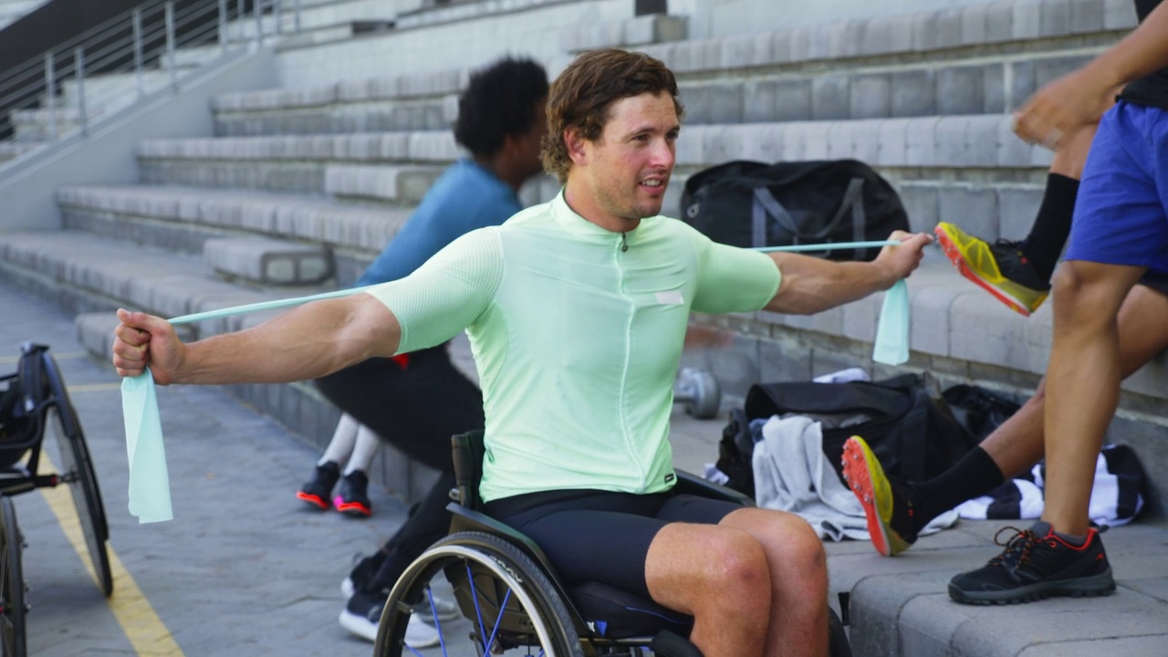 男性轮椅运动员在露天看台用阻力带拉伸视频素材