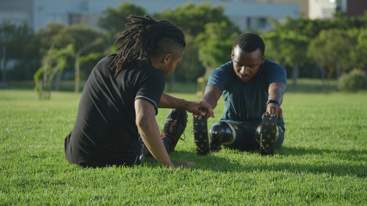 教练和年轻的男性截肢运动员在公园的草地上伸展视频素材