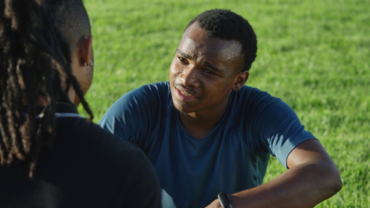 教练和年轻的男性截肢运动员在公园的草地上交谈视频素材
