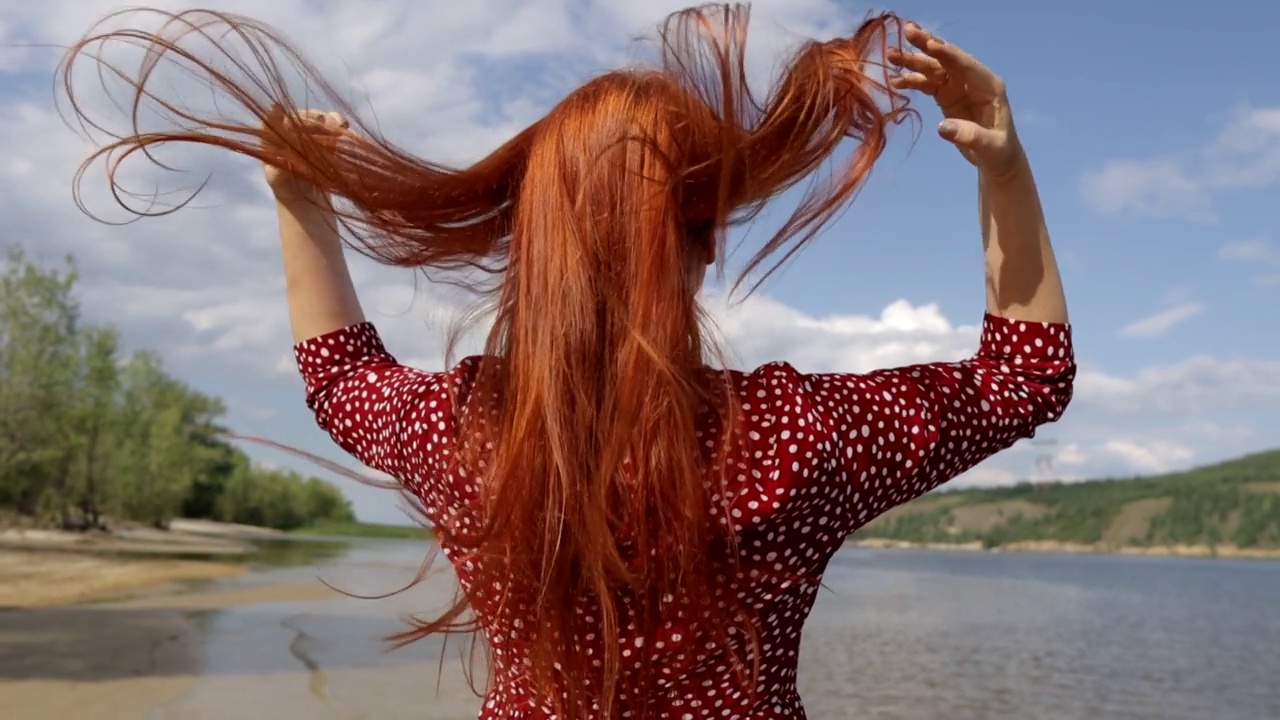 年轻的红头发，美丽的女人穿着红裙子在阳光下干湿的头发，与自然统一的概念。视频素材