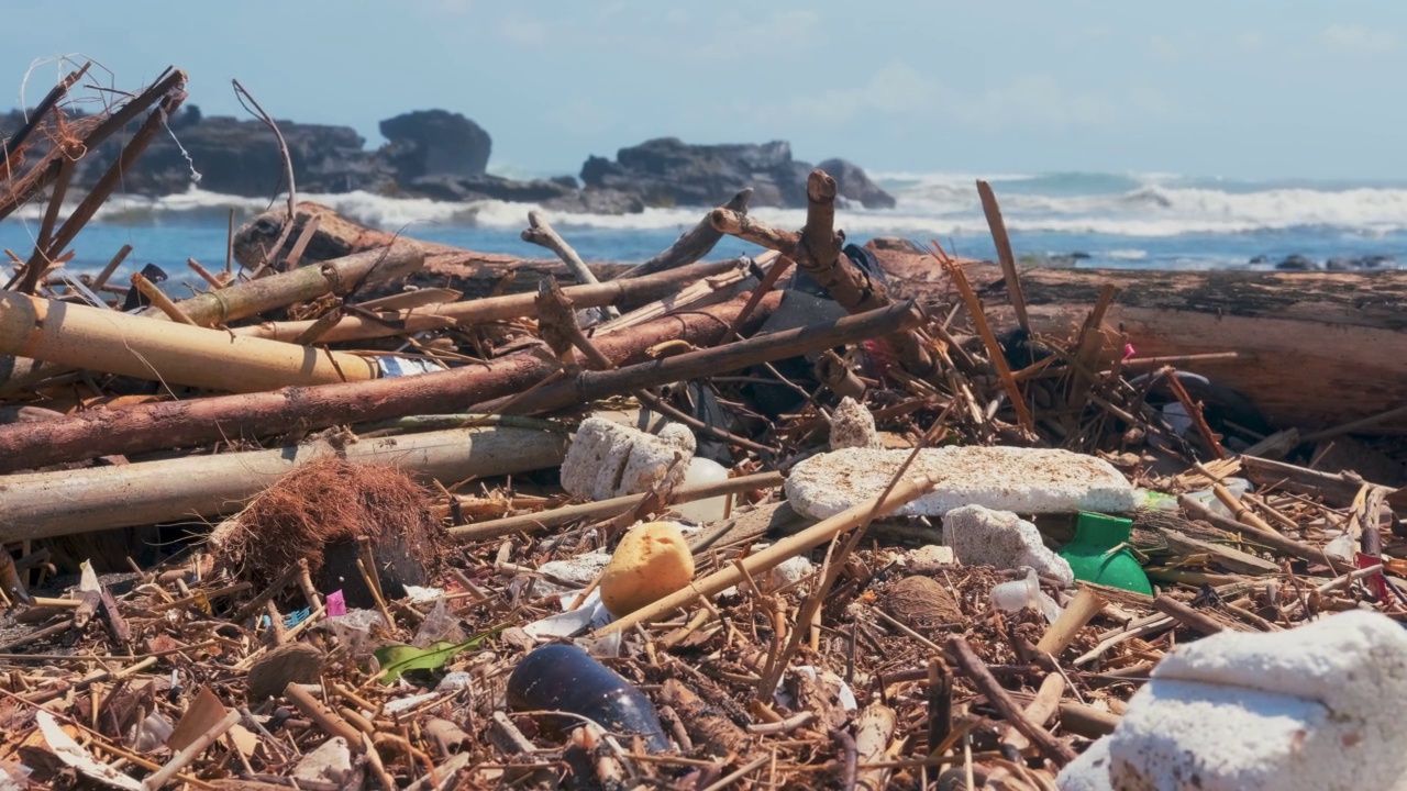 塑料瓶、塑料袋和其他垃圾被倾倒在海洋海滩的深色沙子上。视频素材